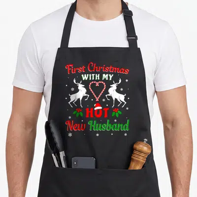 Husband christmas aprons - First Christmas With My Hot New Husband text with reindeer and candy cane heart — shown on a black cotton canvas apron against a white background