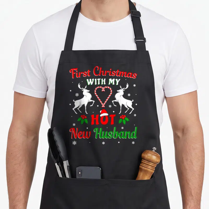 Husband christmas aprons - First Christmas With My Hot New Husband text with reindeer and candy cane heart — shown on a black cotton canvas apron against a white background