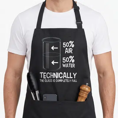 Technically chemistry apron - Beaker diagram with 50% air 50% water text and technically the glass is completely full — shown on a black cotton canvas apron against a white background