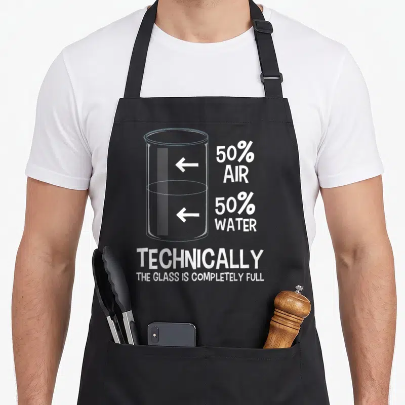 Technically chemistry apron - Beaker diagram with 50% air 50% water text and technically the glass is completely full — shown on a black cotton canvas apron against a white background