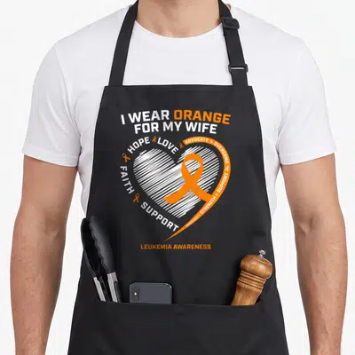 Awareness husband wife aprons - I WEAR ORANGE FOR MY WIFE text with orange ribbon inside hatched white heart — shown on a black cotton canvas apron against a white background