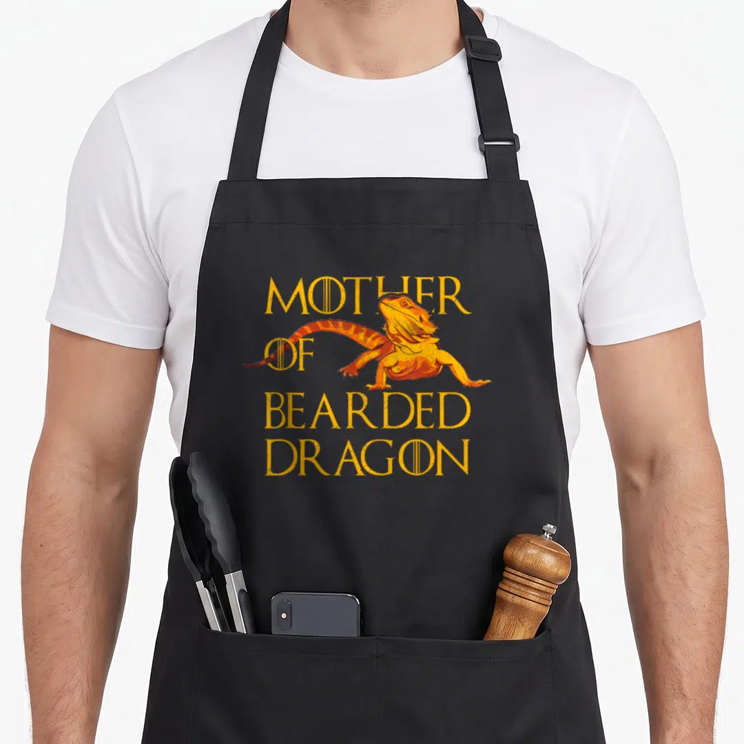 Bearded mother's apron - Cartoon bearded dragon with stacked yellow text reading Mother of Bearded Dragon — shown on a black cotton canvas apron against a white background