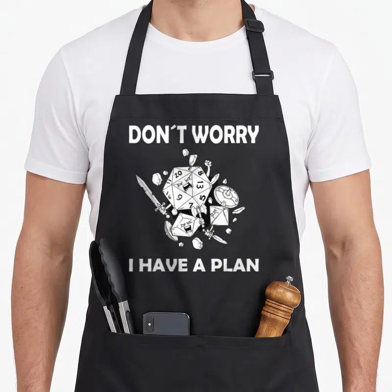 Worry game aprons - Cartoon d20 die and fantasy weapons surrounded by debris with text Don't Worry I Have A Plan — shown on a black cotton canvas apron against a white background