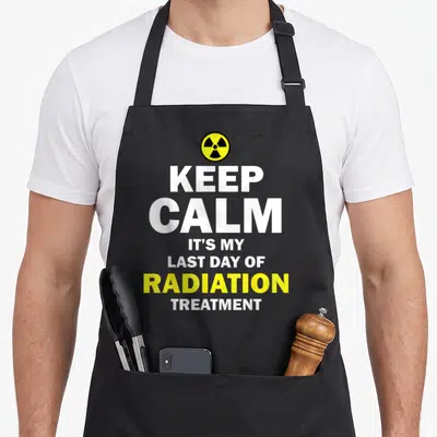 Cute therapy radiation aprons - Yellow radiation symbol above white and yellow stacked text reading KEEP CALM IT'S MY — shown on a black cotton canvas apron against a white background