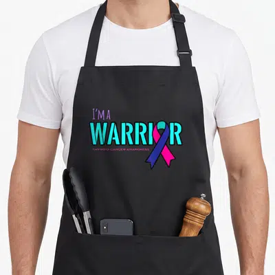 Awareness thyroid apron - I'm a Warrior text with cyan purple pink blue ribbon overlapping the letter O — shown on a black cotton canvas apron against a white background