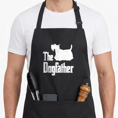 Scottish dog dad apron - White The Dogfather text with Scottish Terrier silhouette — shown on a black cotton canvas apron against a white background