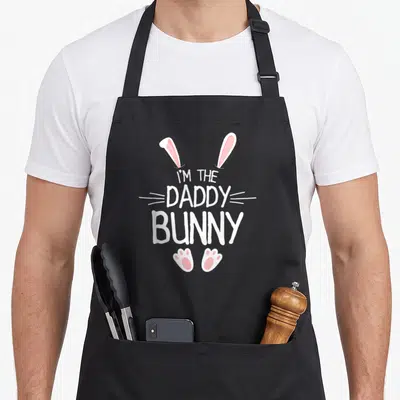 Cute family easter bunny aprons - White and pink cartoon bunny ears paws and whiskers surrounding I'M THE DADDY BUNNY — shown on a black cotton canvas apron against a white background