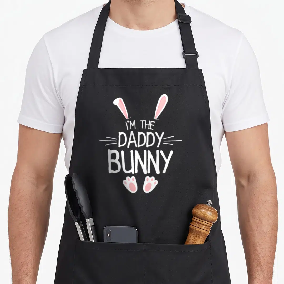 Cute family easter bunny aprons - White and pink cartoon bunny ears paws and whiskers surrounding I'M THE DADDY BUNNY — shown on a black cotton canvas apron against a white background