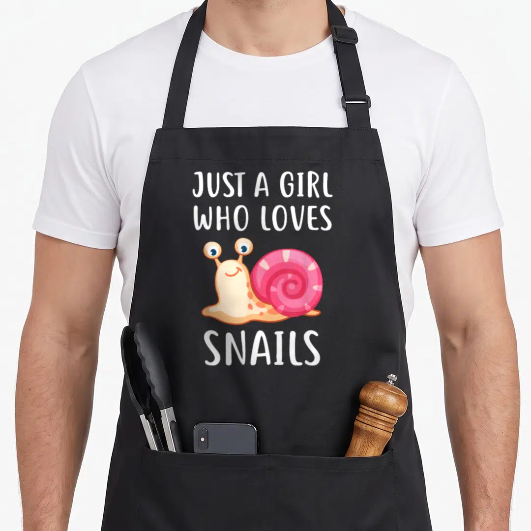 Cute snail apron - Cartoon snail with pink shell and white text Just A Girl Who Loves Snails — shown on a black cotton canvas apron against a white background