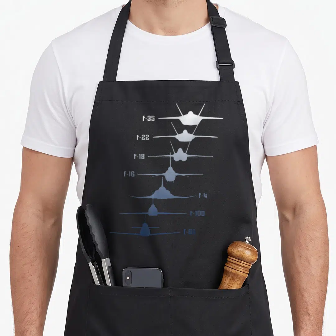 F35 f18 apron - Seven fighter jets stacked vertically labeled F-35 F-22 F-18 F-16 F-4 F-100 F-86 in white and blue — shown on a black cotton canvas apron against a white background