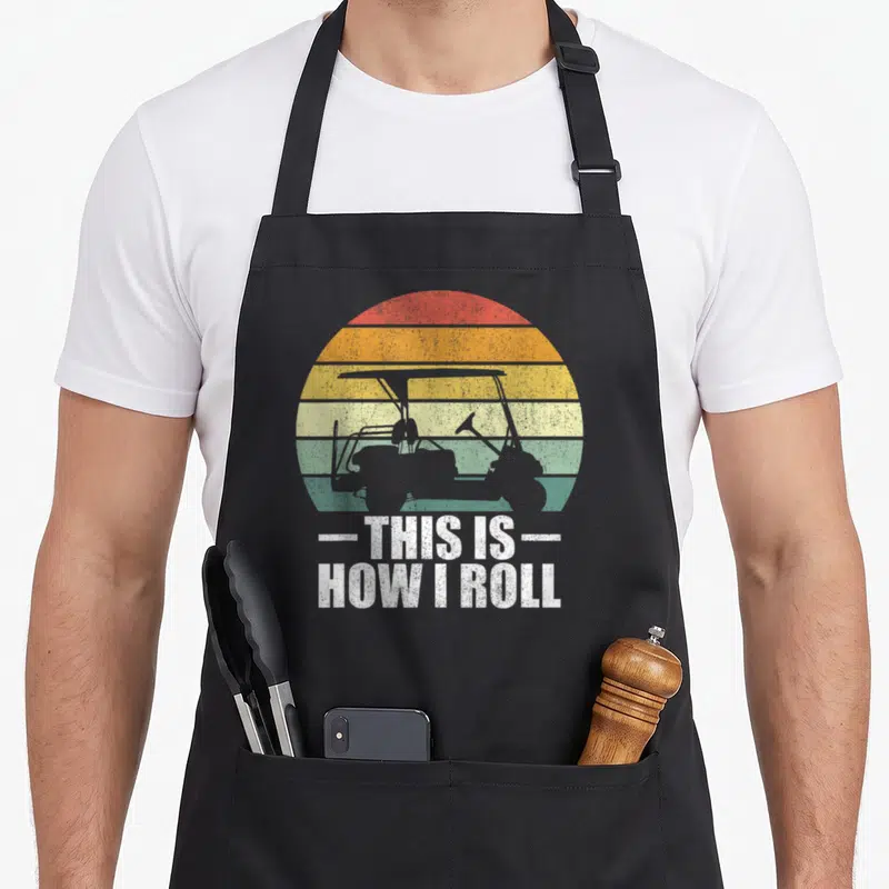 Roll golfer golf apron - Golf cart silhouette over red orange yellow green striped sun with white text THIS IS HOW I — shown on a black cotton canvas apron against a white background