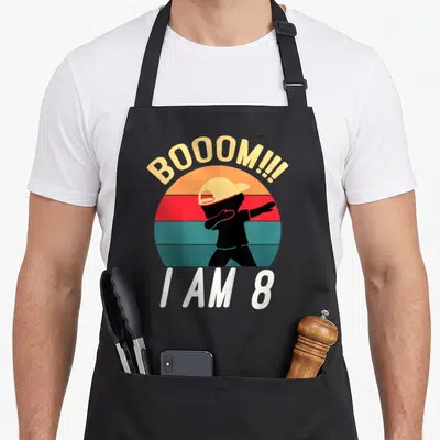 Outfit birthday apron - Dabbing silhouette in front of striped sun with BOOOM and I AM 8 text — shown on a black cotton canvas apron against a white background