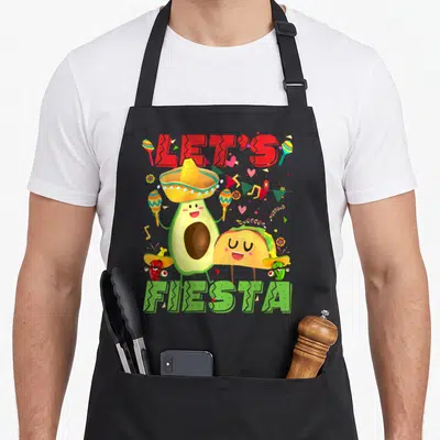Avocado mexican apron - Cartoon avocado, taco, and peppers in sombreros holding maracas under Let's Fiesta text — shown on a black cotton canvas apron against a white background