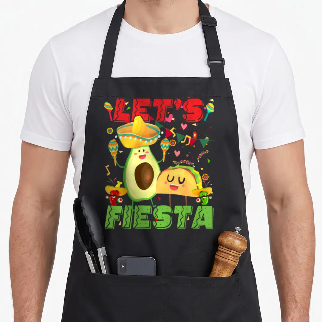 Avocado mexican apron - Cartoon avocado, taco, and peppers in sombreros holding maracas under Let's Fiesta text — shown on a black cotton canvas apron against a white background