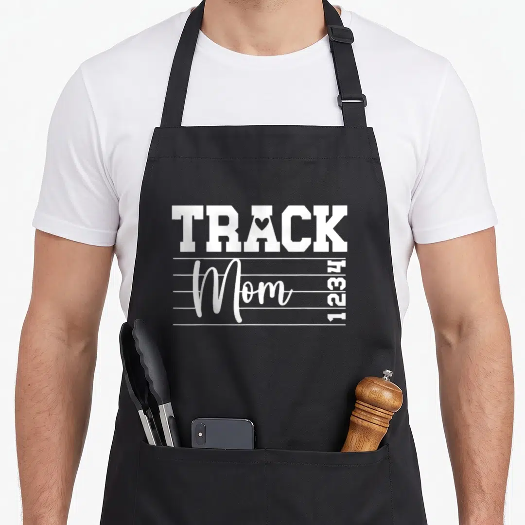 Field mother's apron - White TRACK Mom text with heart in A, four horizontal lines, and vertical 1234 numbers — shown on a black cotton canvas apron against a white background