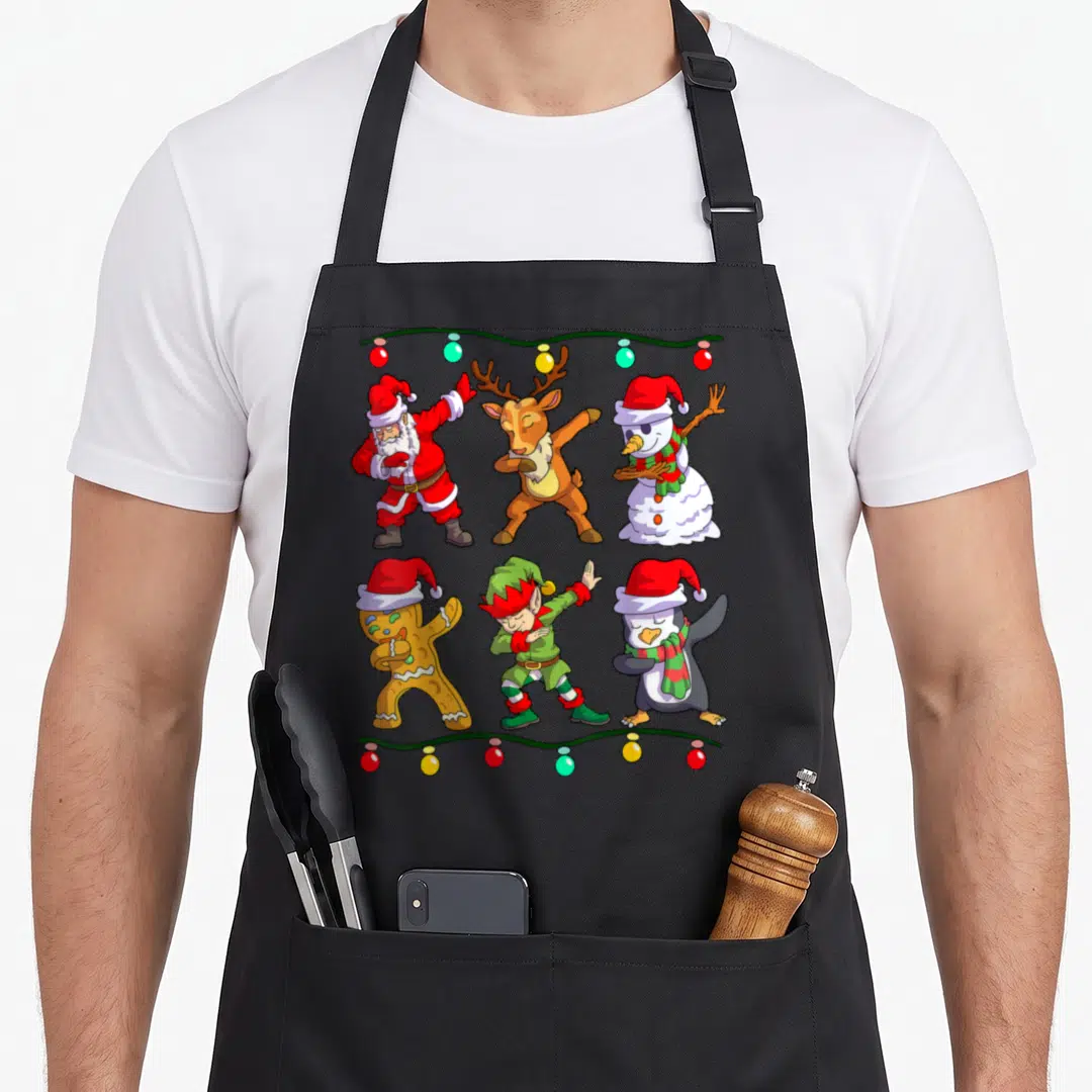 Dabbing elf apron - Six cartoon Christmas characters dabbing framed by red and green string lights — shown on a black cotton canvas apron against a white background