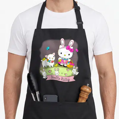 Scene easter apron - Hello Kitty holding egg basket with lamb chicks bunnies pink ribbon text — shown on a black cotton canvas apron against a white background