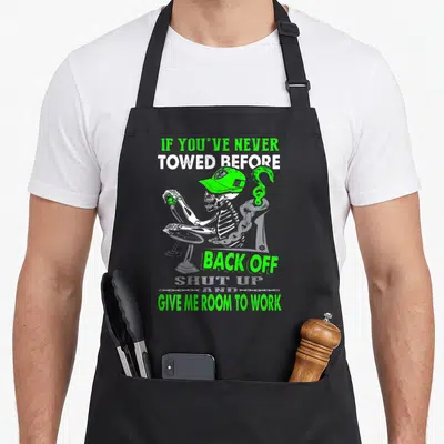 Operator truck apron - Cartoon skeleton in green cap with tow hook and sarcastic text about giving room to work — shown on a black cotton canvas apron against a white background