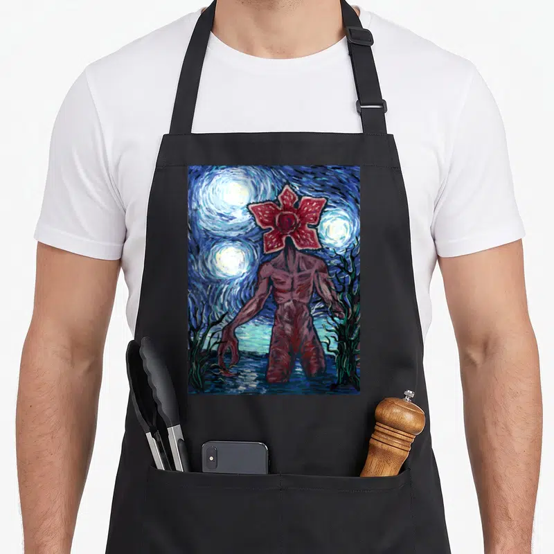 Demogorgon starry night apron - Red flower-headed monster in swirling blue night sky with yellow stars watercolor style — shown on a black cotton canvas apron against a white background