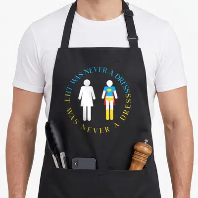 Power superhero apron - Two minimalist figures, one in dress and one in superhero gear, surrounded by circular text — shown on a black cotton canvas apron against a white background