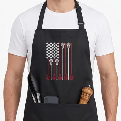 Lacrosse stick american flag apron - Red and white lacrosse sticks and circles arranged in a US flag pattern — shown on a black cotton canvas apron against a white background