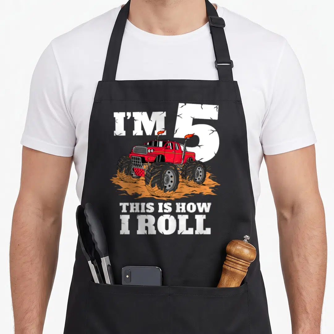 5th truck apron - Red monster truck over orange dirt with I'M 5 THIS IS HOW I ROLL text — shown on a black cotton canvas apron against a white background