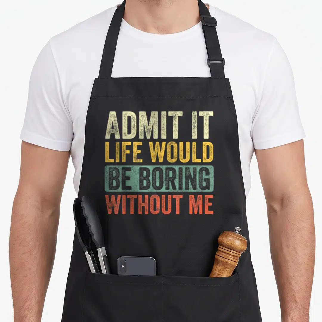 Would novelty apron - Stacked retro typography reading Admit It Life Would Be Boring Without Me in beige yellow grey — shown on a black cotton canvas apron against a white background