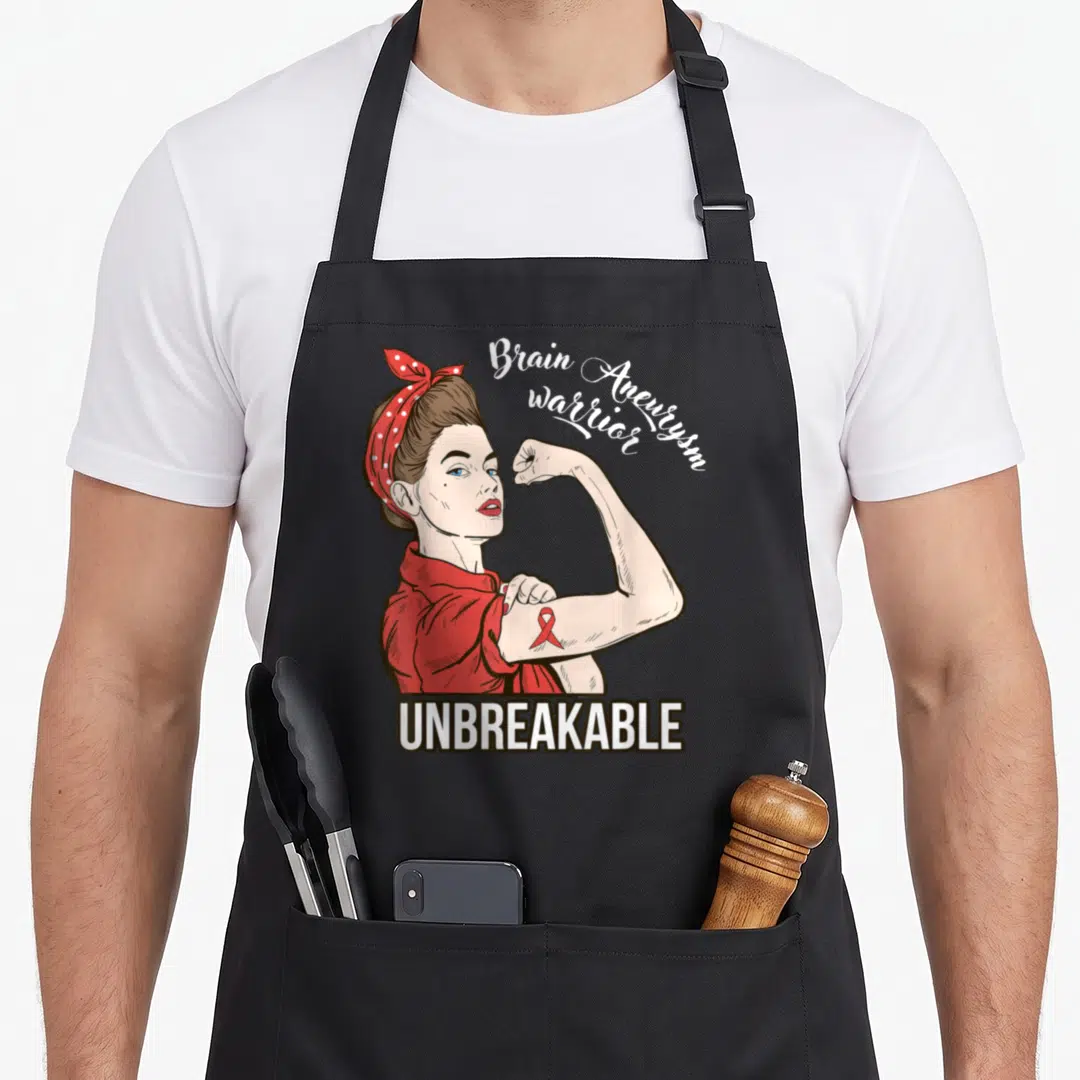 Warrior aneurysm awareness apron - Cartoon woman flexing arm with red ribbon and text Brain Aneurysm warrior UNBREAKABLE — shown on a black cotton canvas apron against a white background
