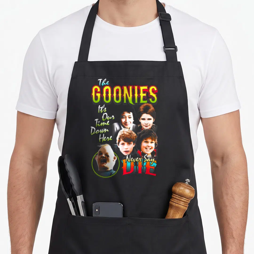 Edit character aprons - The Goonies title, four boy faces, One Eyed Willy portrait, and movie quotes in yellow red blue — shown on a black cotton canvas apron against a white background