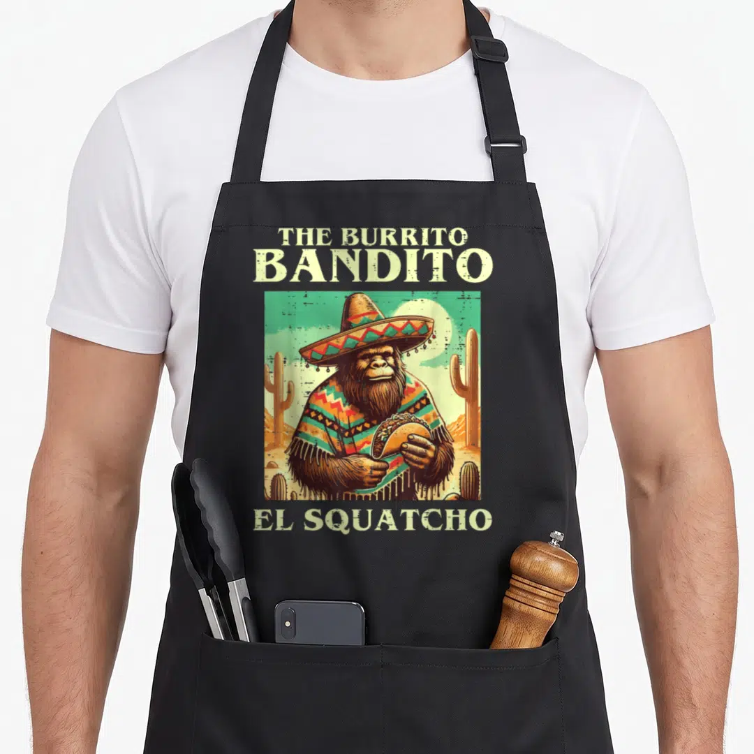 Sasquatch mexican apron - Cartoon sasquatch in sombrero holding burrito with text The Burrito Bandito El Squatcho — shown on a black cotton canvas apron against a white background