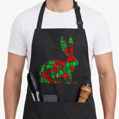 Bunny christmas tree apron - Rabbit silhouette filled with red and green Christmas icons like trees and snowflakes — shown on a black cotton canvas apron against a white background