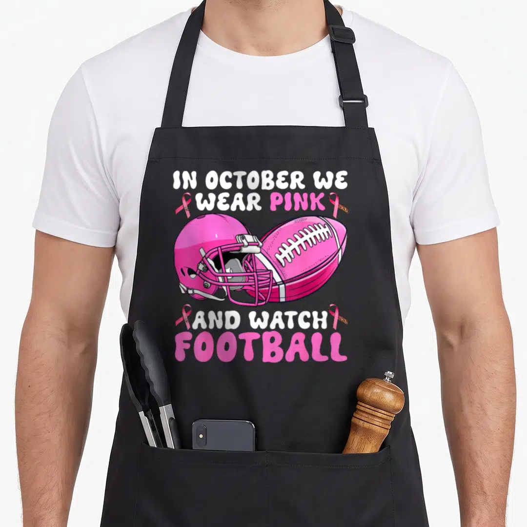 Football breast cancer awareness aprons - Pink helmet football and ribbons with IN OCTOBER WE WEAR PINK text — shown on a black cotton canvas apron against a white background