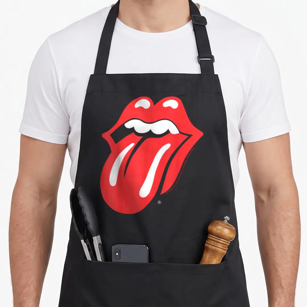 Funny tongue rolling stones apron - Red cartoon mouth with protruding tongue and white teeth on grey background — shown on a black cotton canvas apron against a white background