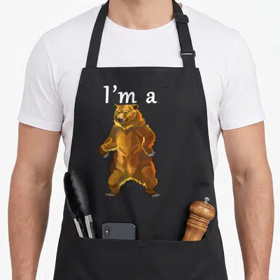 Funny grizzly bear apron - Standing brown cartoon bear with white 'I'm a' text above — shown on a black cotton canvas apron against a white background