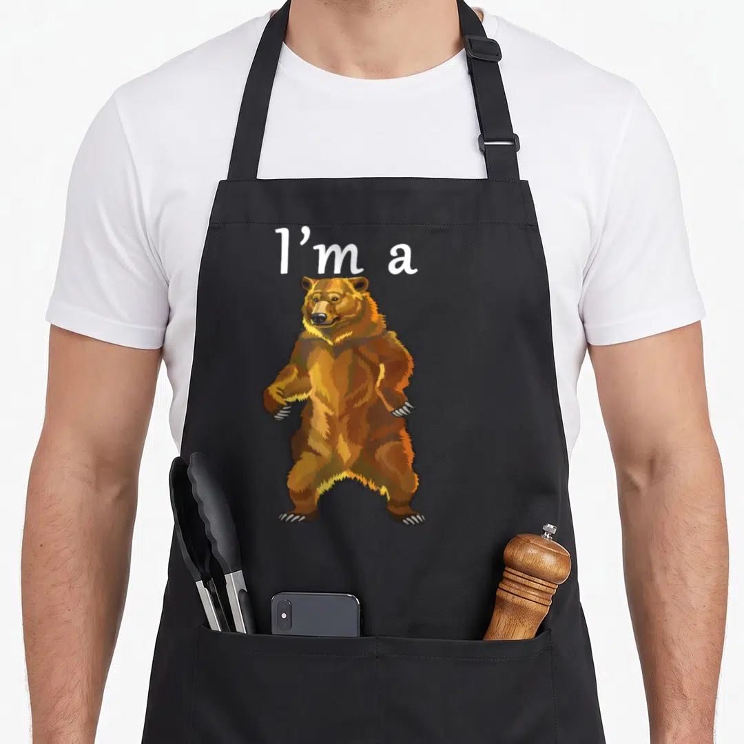 Funny grizzly bear apron - Standing brown cartoon bear with white 'I'm a' text above — shown on a black cotton canvas apron against a white background
