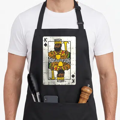 Card african print apron - Retro King of Spades playing card design in yellow brown white and black — shown on a black cotton canvas apron against a white background