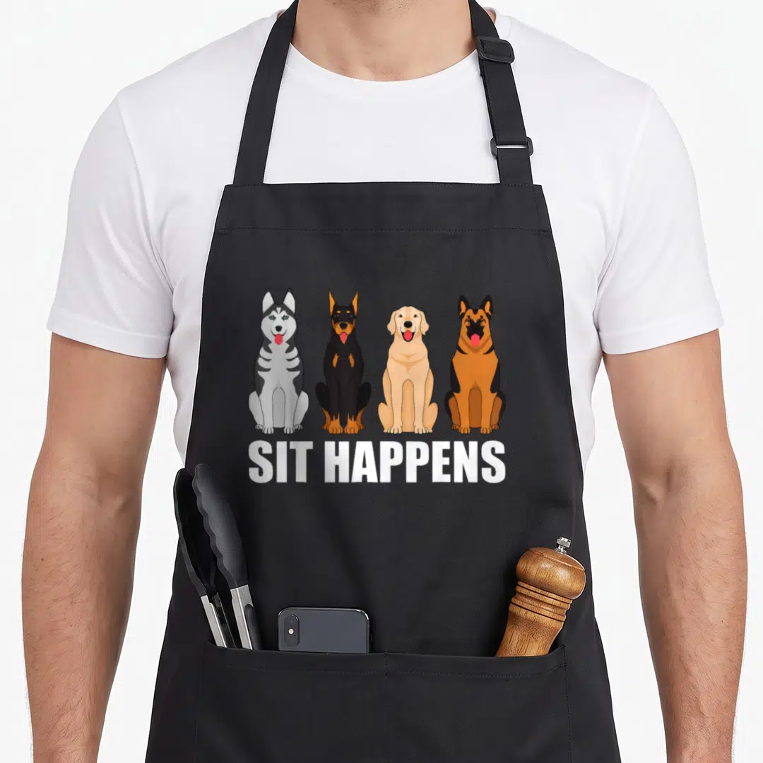 Pet dog training apron - Four cartoon dogs sitting in a row above white SIT HAPPENS text on a grey background — shown on a black cotton canvas apron against a white background