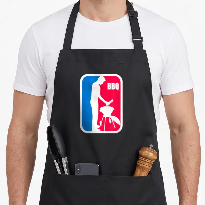 League barbecue apron - White man grilling silhouette on split blue red background with BBQ text — shown on a black cotton canvas apron against a white background