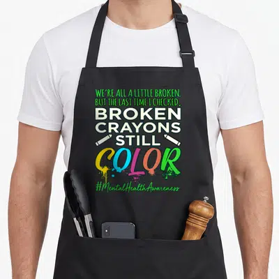 Broken ptsd awareness apron - Stacked text reading broken crayons still color with two white crayons and multi-colored — shown on a black cotton canvas apron against a white background