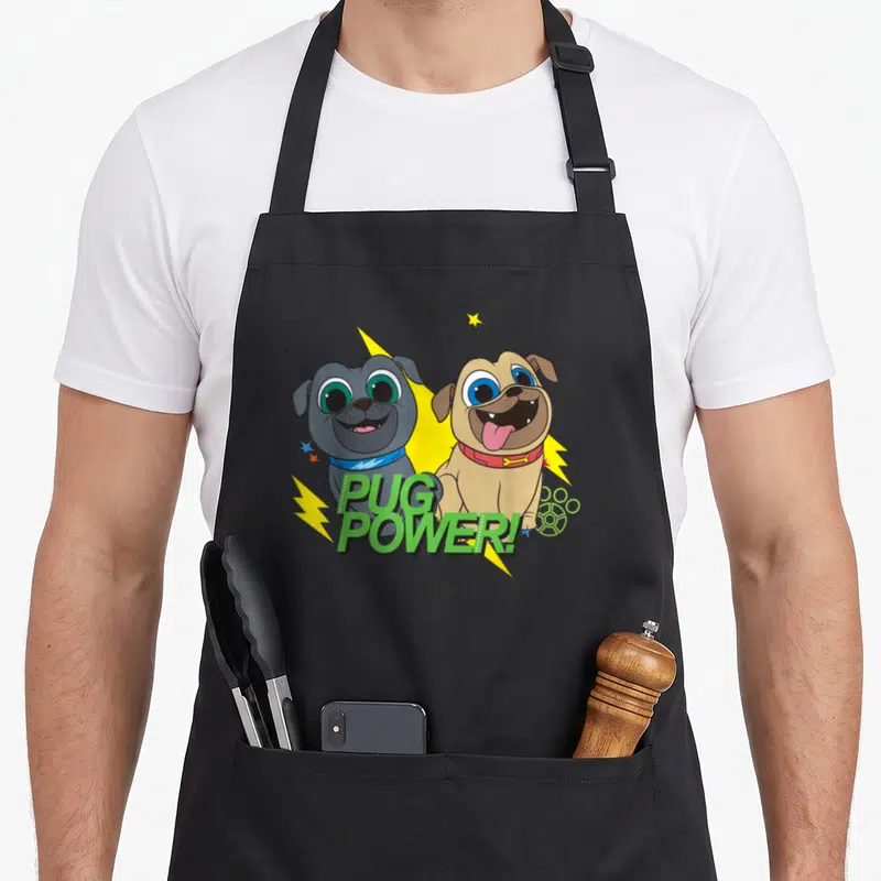 Power dog apron - Two cartoon pugs, grey and tan, with yellow lightning bolts and green PUG POWER! text — shown on a black cotton canvas apron against a white background