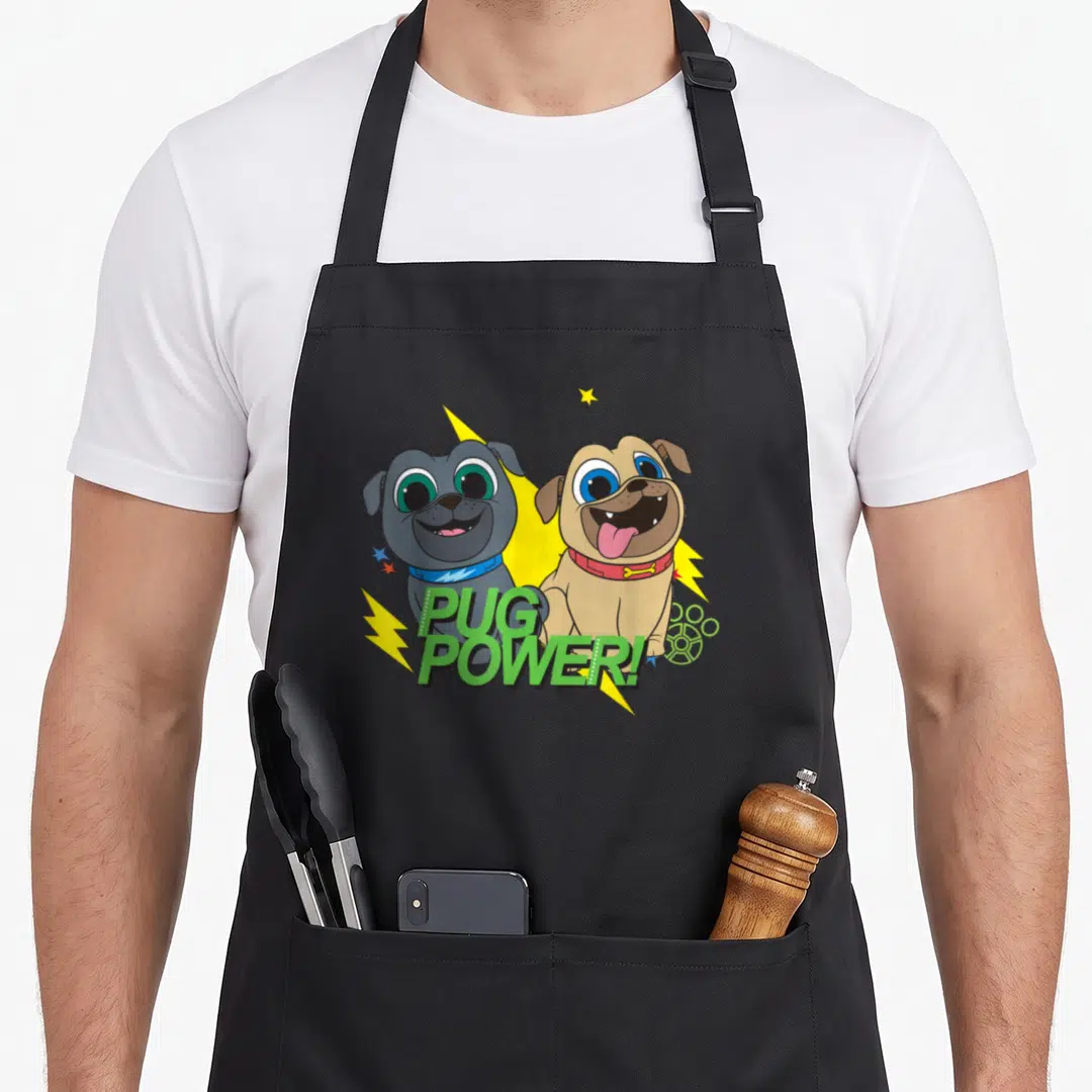 Power dog apron - Two cartoon pugs, grey and tan, with yellow lightning bolts and green PUG POWER! text — shown on a black cotton canvas apron against a white background
