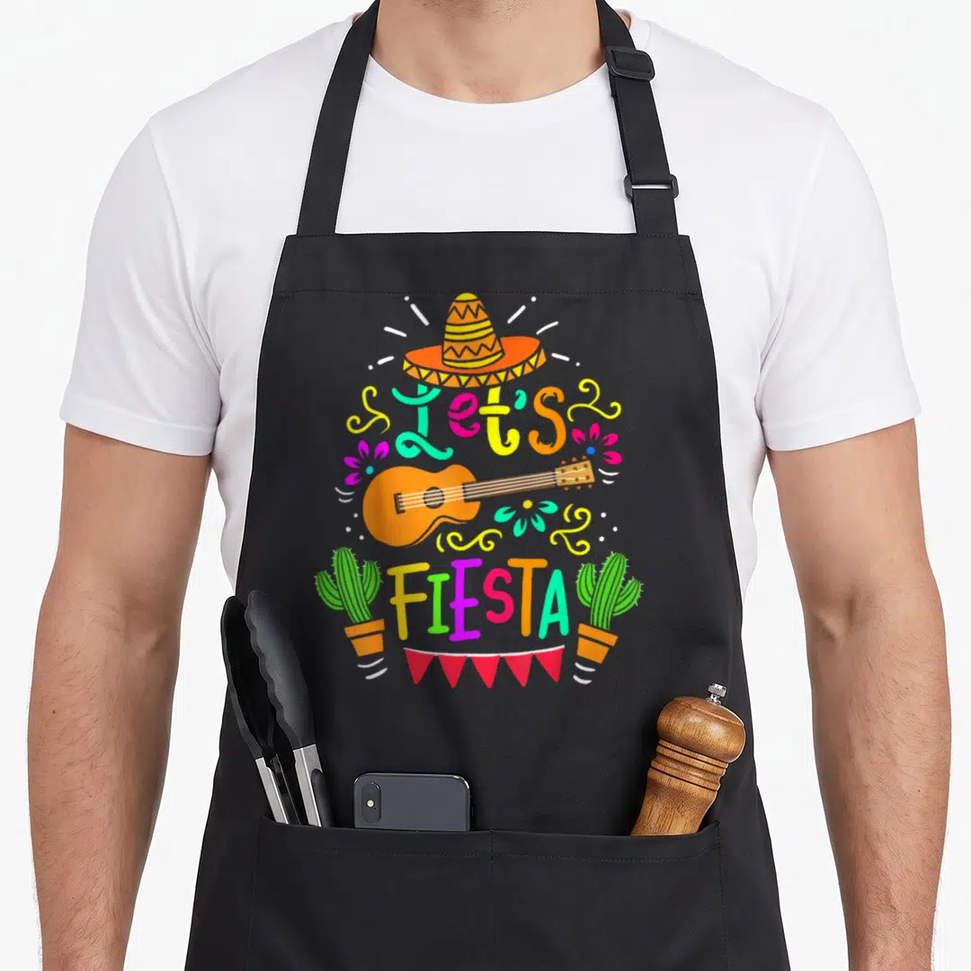 Cinco mexican apron - Orange guitar, sombrero, Let's FIESTA text, potted cacti, and red bunting in bright colors — shown on a black cotton canvas apron against a white background
