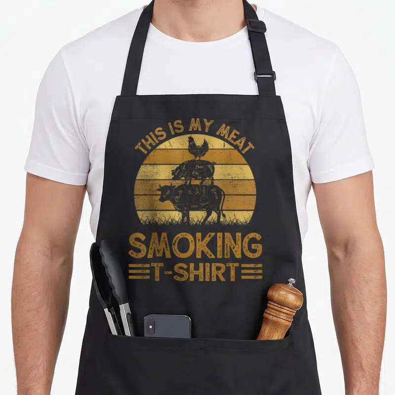 Smoking meat aprons - Orange distressed sun with stacked chicken pig cow silhouettes and THIS IS MY MEAT SMOKING — shown on a black cotton canvas apron against a white background