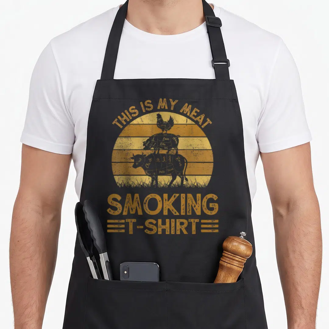 Smoking meat aprons - Orange distressed sun with stacked chicken pig cow silhouettes and THIS IS MY MEAT SMOKING — shown on a black cotton canvas apron against a white background