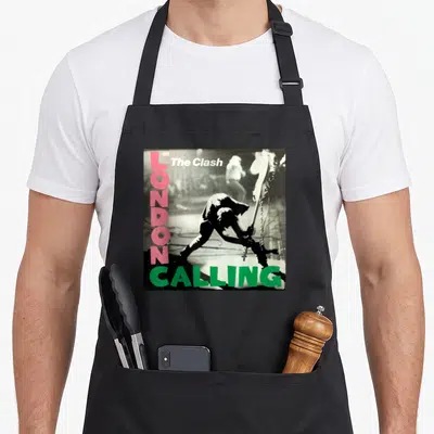 Clash london aprons - Black silhouette figure with guitar, vertical pink LONDON text, green CALLING text, white band — shown on a black cotton canvas apron against a white background