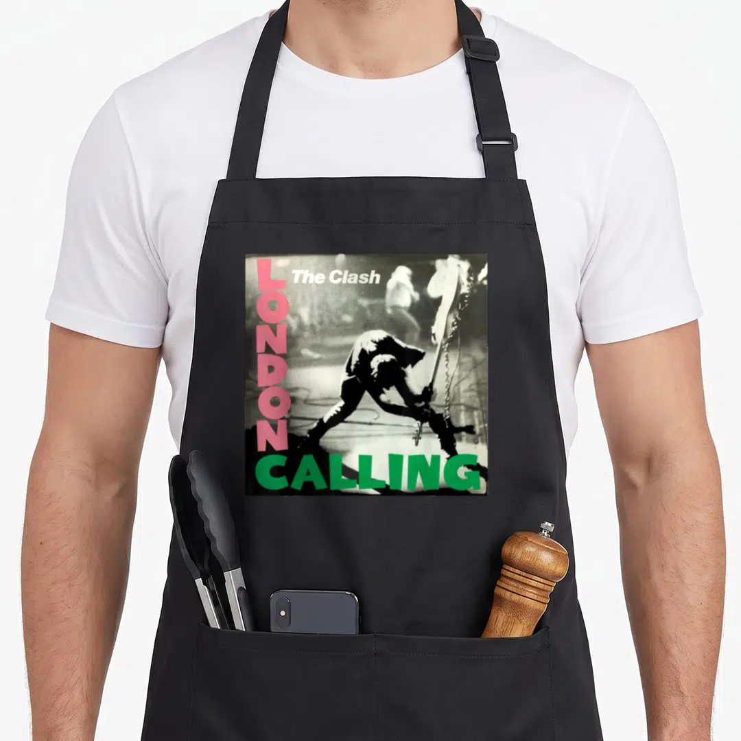 Clash london aprons - Black silhouette figure with guitar, vertical pink LONDON text, green CALLING text, white band — shown on a black cotton canvas apron against a white background