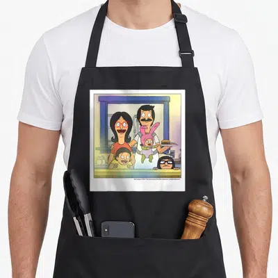 Belcher bobs burger apron - Belcher family cartoon behind counter with burger, yellow blue pink red colors — shown on a black cotton canvas apron against a white background