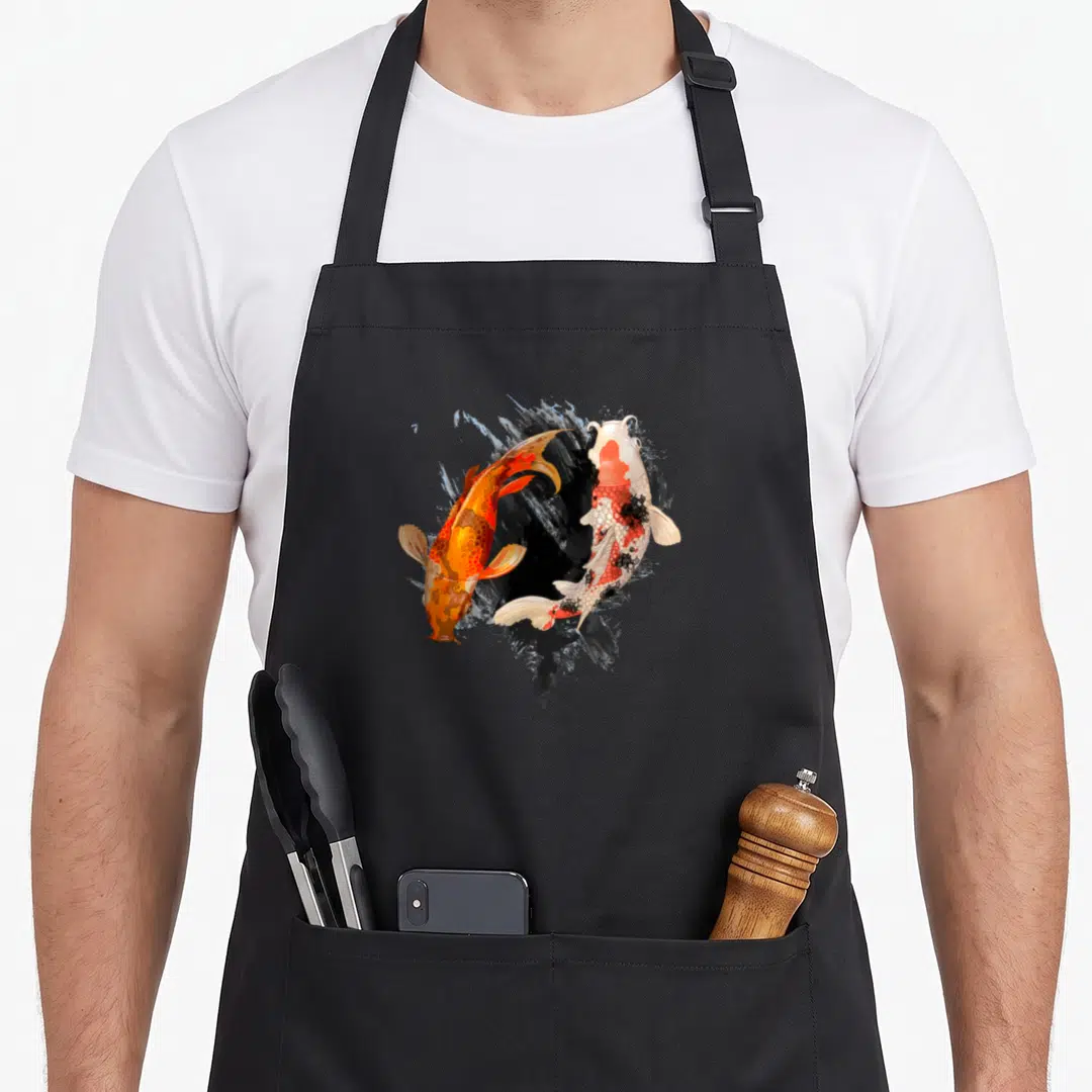 Koi japan apron - Two realistic koi fish, one orange and one white with red markings, swimming over black and blue-grey — shown on a black cotton canvas apron against a white background