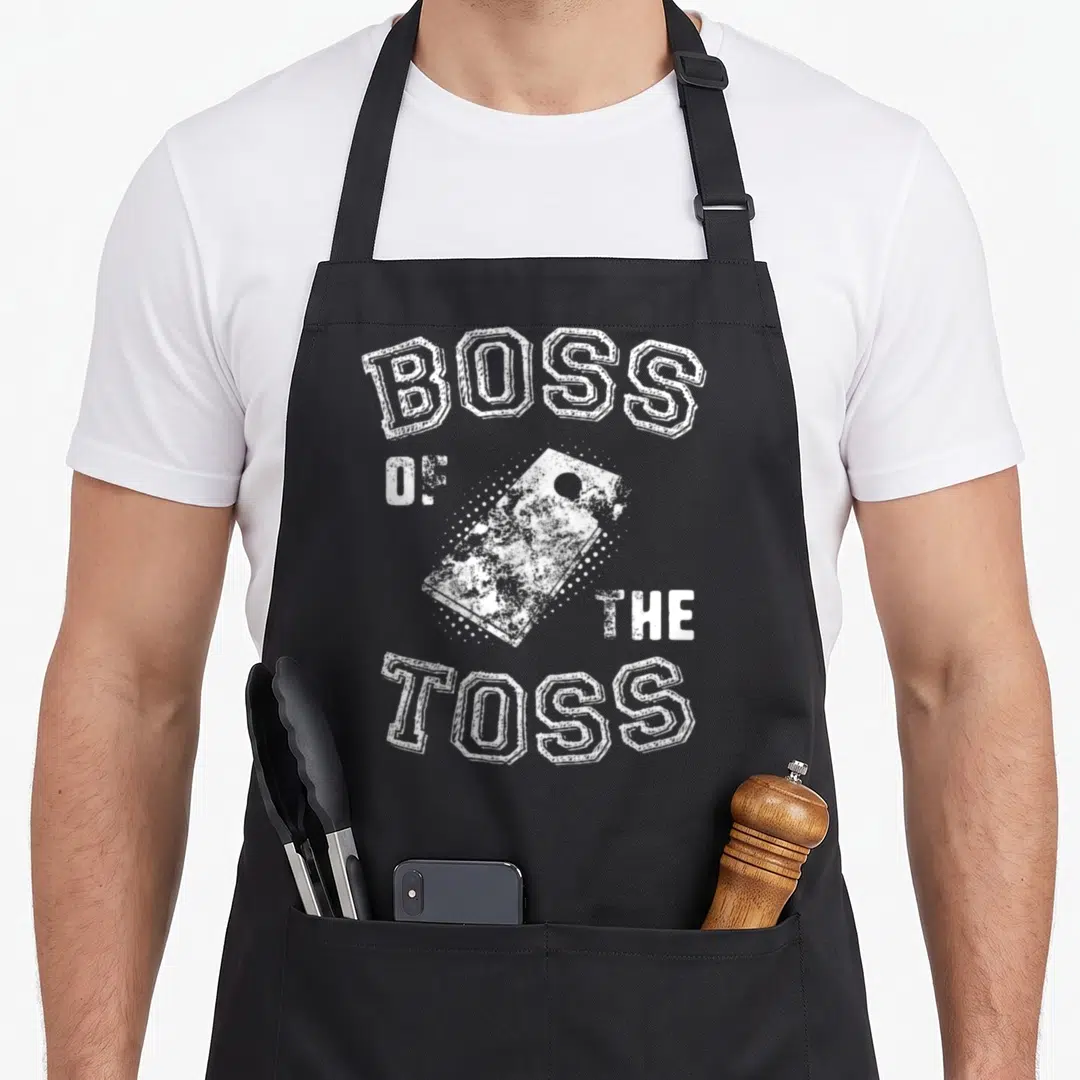Cornhole distressed apron - White distressed bean bag surrounded by BOSS OF THE TOSS block letters — shown on a black cotton canvas apron against a white background