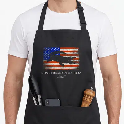Ron florida apron - Grey alligator on distressed flag with text DONT TREAD ON FLORIDA and signature watermark — shown on a black cotton canvas apron against a white background